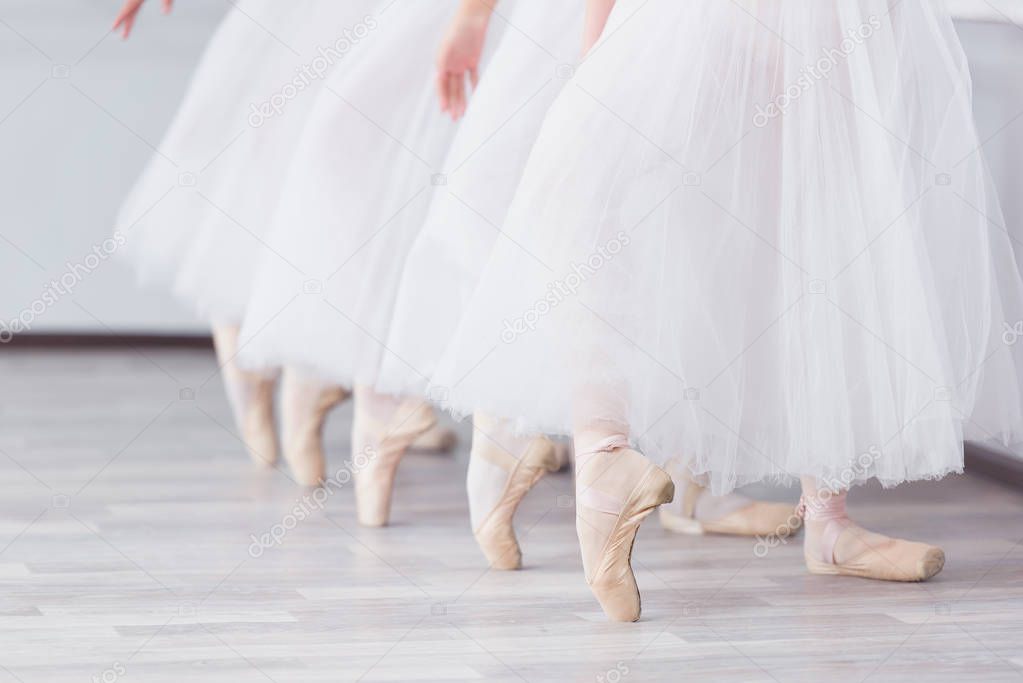 Feet in pointe. Exercises in the ballet school. Ballet classes. A group of girls standing in a row, stretched out their legs, shod in pointe. Children in white skirts. The teacher leads a dance lesson.