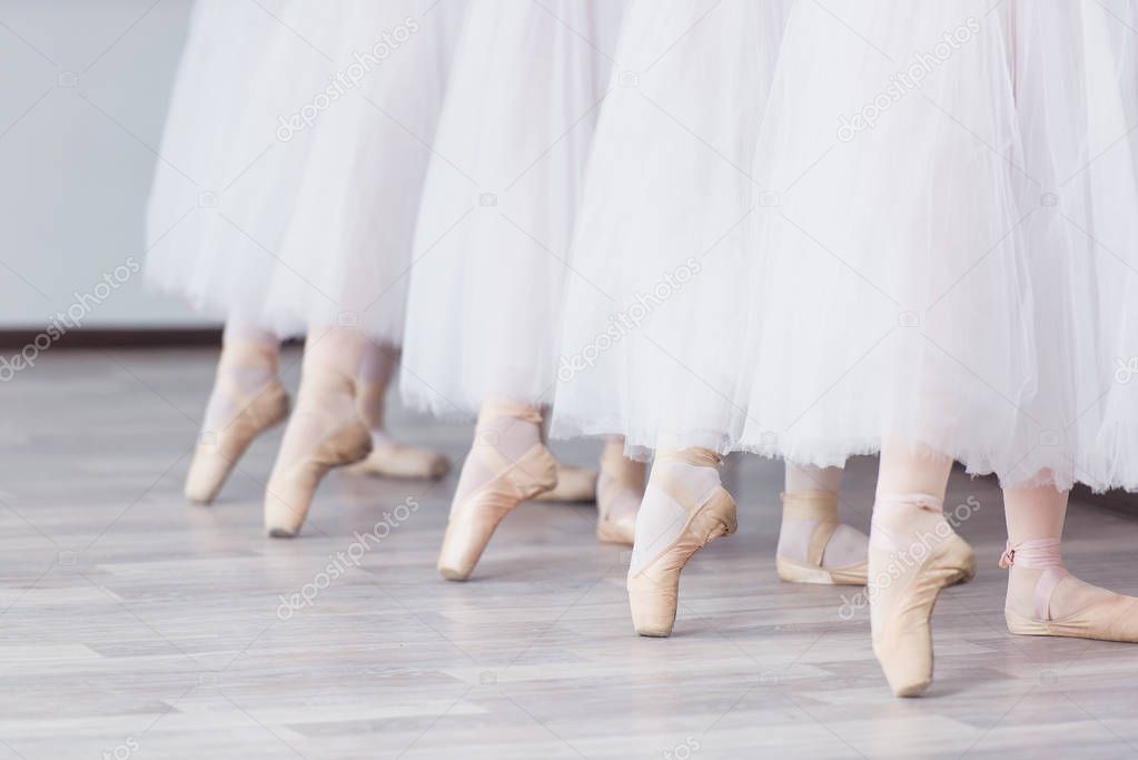 Feet in pointe. Exercises in the ballet school. Ballet classes. A group of girls standing in a row, stretched out their legs, shod in pointe. Children in white skirts. The teacher leads a dance lesson.