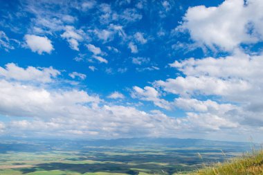 Mavi gökyüzü bulutlu. Dağlarda güneşli bir gün. Bitki örtüsü dağ yamaçlarında. Kır çiçekleri. Engebeli arazi. Yeşil çimen.