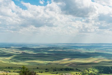 Mavi gökyüzü ile kabarık bulutlar. Beyaz cirrus bulutlar güneş tarafından aydınlatılmış. Yeşil Yayla küçük tepelerde. Dünya gökyüzü karşılamaktadır. Dünya havadan görünümü. Ufuk uzak. Bulutların altında güzel düz.