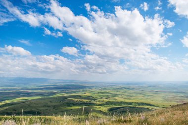 Mavi gökyüzü ile kabarık bulutlar. Beyaz cirrus bulutlar güneş tarafından aydınlatılmış. Yeşil Yayla küçük tepelerde. Dünya gökyüzü karşılamaktadır. Dünya havadan görünümü. Ufuk uzak. Bulutların altında güzel düz.
