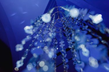 Cam kolye. Yuvarlak düz boncuk metal tabanından asmak. Mavi ışık. İç cam aksesuar. Boncuk bir satır askıda daire etrafında bağlı. Üst üste asılı cam boncuklar.