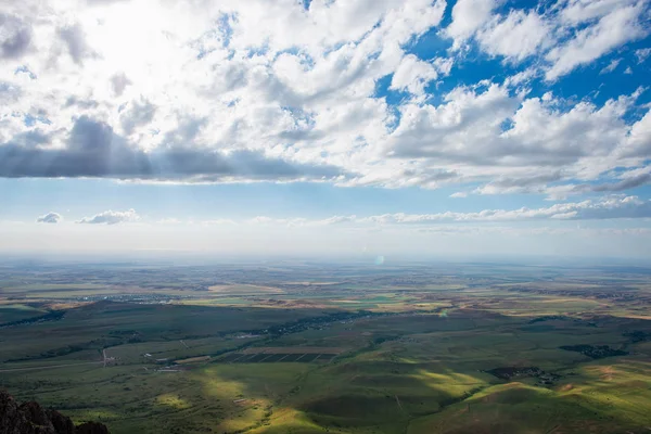 stock image Blue sky with fluffy clouds. White cirrus clouds illuminated by the sun. Greenery small hills on the plateau. Earth meets the sky. Earth aerial view. Horizon away. Beautiful plain under the clouds.