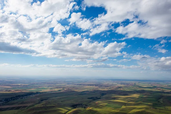 Blue sky with fluffy clouds. White cirrus clouds illuminated by the sun. Greenery small hills on the plateau. Earth meets the sky. Earth aerial view. Horizon away. Beautiful plain under the clouds.