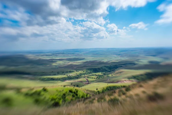 Blue sky with fluffy clouds. White cirrus clouds illuminated by the sun. Greenery small hills on the plateau. Earth meets the sky. Earth aerial view. Horizon away. Beautiful plain under the clouds.