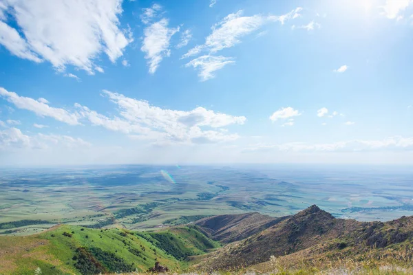 Blue sky with fluffy clouds. White cirrus clouds illuminated by the sun. Greenery small hills on the plateau. Earth meets the sky. Earth aerial view. Horizon away. Beautiful plain under the clouds.