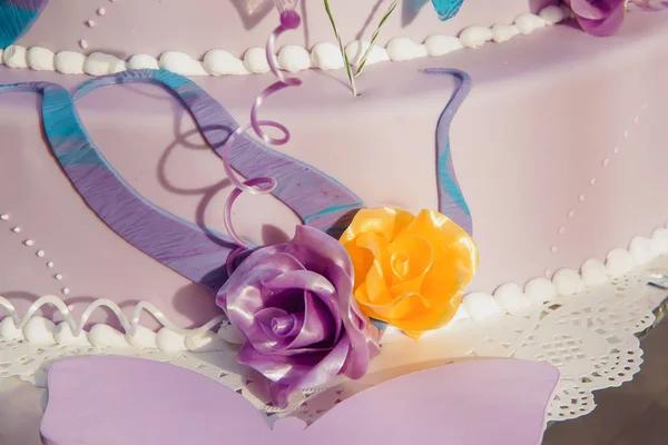 Three-story cake in purple glaze. Cake decoration. Multicolored butterflies from glaze. Purple and yellow roses from mastic. Sweet pastries. Dessert.