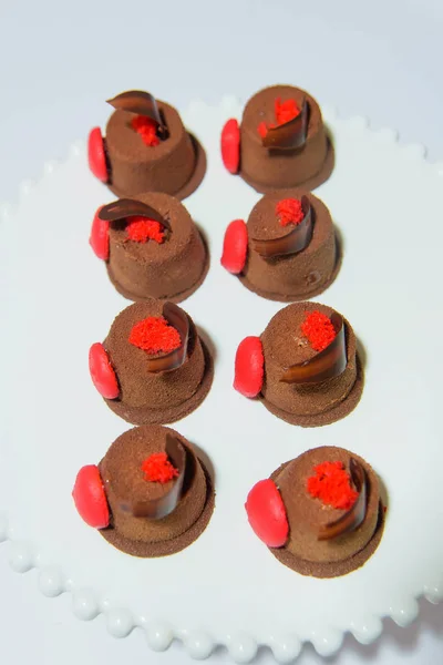 Chocolate mini cakes with red candy. Cakes on a white background. Cakes under the name: Petit four. Sweet pastries. Desserts: Petit Fours.