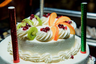 Çift güverte pasta beyaz. Tatlı hamur işleri. Pasta Portakal ve kivi ile dekore edilmiştir. Havai fişek kek üzerine mumlar. Tatlı. Tereyağı krema. Bisküvi.