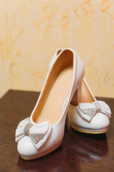 Wedding women\'s shoes. White shoes. Wedding. Shoes standing on a wooden bedside table. Shoes decorated with bows.