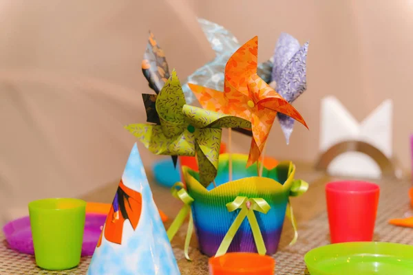 Children\'s birthday. Colorful bright dishes on the table. Paper windmills on sticks. Color holiday caps on the head. Windmill.