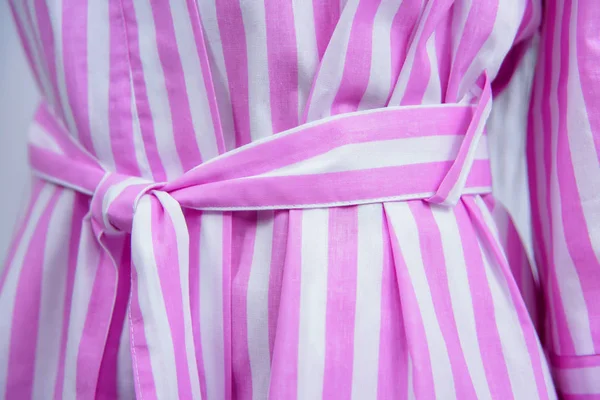 Cotton bathrobe. Textile. Dressing gown of pink color in a white strip. The texture of the fabric. Cotton. Robe belt People. Clothes for hotels and hotels. Woman. Dark hair. Arm.