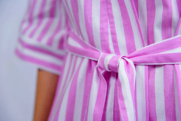 Cotton bathrobe. Textile. Dressing gown of pink color in a white strip. The texture of the fabric. Cotton. Robe belt People. Clothes for hotels and hotels. Woman. Dark hair. Arm.