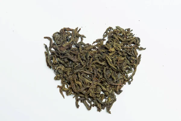 Leaf tea laid out in the shape of a heart on a white background. Leaf tea storage. Natural product. Weighted green tea. Packing and sorting.