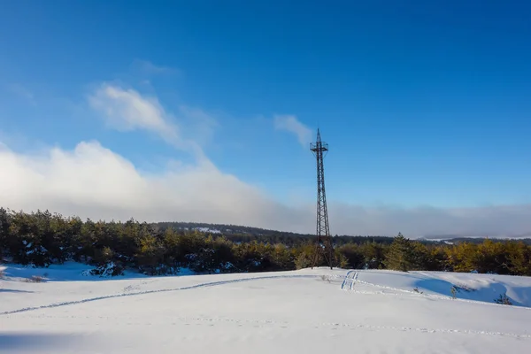 Snow-covered hills of the mountains. Pines in the snow. Blue sky. Thick white clouds. Height above sea level. Mountain called: Ai-Petri. Crimean mountains. Metal radio tower. Tourism. Rest in Crimea. Winter.