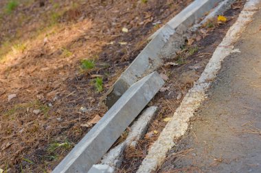 Yola yakın kenarlık. Beton kaldırım yanlış yerde kendi tarafında yatıyor. Bozuk yol parkta. Yanındaki kaldırım taş döşeme. Kaldırıma onun yerden kaldırıldı.