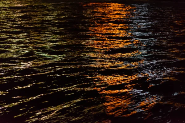 The lights of the night city are reflected in the water. Ripples on the surface of the water. Night time. View of the sea at night. Water texture. Beautiful reflection. Black Sea.