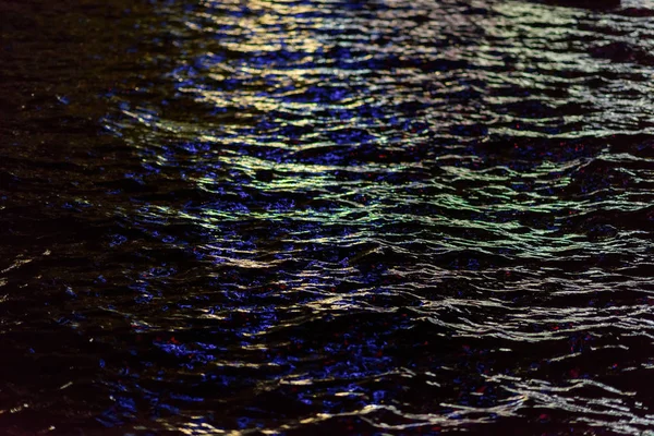 The lights of the night city are reflected in the water. Ripples on the surface of the water. Night time. View of the sea at night. Water texture. Beautiful reflection. Black Sea.