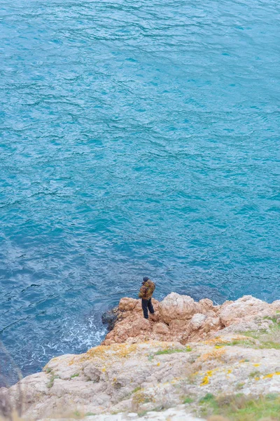 Embankment Balaclava Man Fisherman Catches Fish Blue Water Rocky Coast — Stock Photo, Image