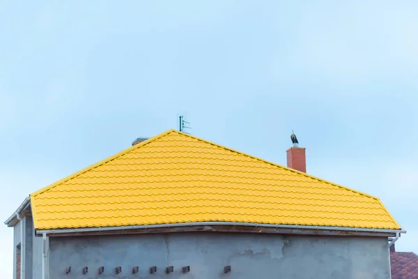 Metal tile yellow. House roof. Blue sky. Construction. Roofing material. Thin sheets of steel. Protective metal coating.