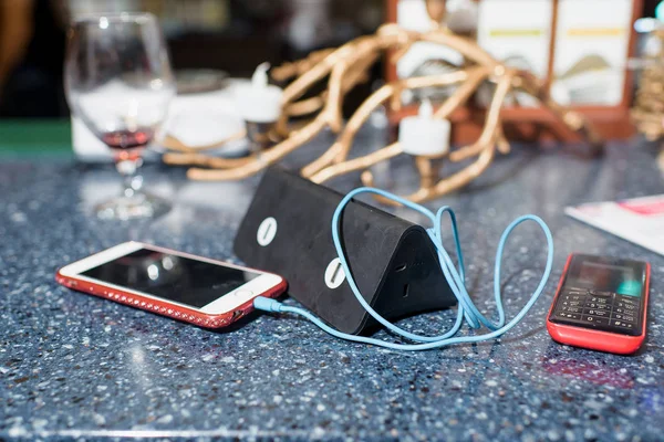 Smartphone white. Phone. The power cable for the phone. The wire is blue. Glass wine glass. Marble table. Portable charging. Gadget.