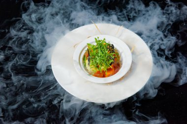 Sıvı azot ile yemekleri sunan. Sebze ve roka salatası. Vejetaryen yemek. Domates ve salatalık. Beyaz bir seramik tabak taze salata. Siyah bir arka plan üzerinde çanak.