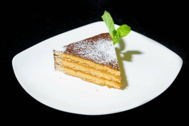 Tatlı Tiramisu. Kek. Tatlı hamur işleri. Şekerlemeler. Pasta krema şeker ile silkeledi. Nane taze yeşil yaprak. Güzel tatlı hizmet. Siyah bir arka plan üzerinde beyaz bir tabak içinde tiramisu.