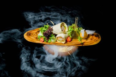 Sıvı azot ile yemekleri sunan. Pide tavuk rulo. Sebze ve salata yaprakları. Yemekler için ahşap tahta. Pide tavuk. Taze salata. Bir dilim limon. Bir cam şişe zeytinyağı.