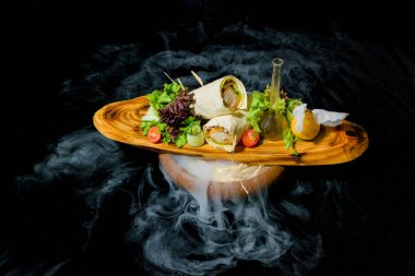 Sıvı azot ile yemekleri sunan. Pide tavuk rulo. Sebze ve salata yaprakları. Yemekler için ahşap tahta. Pide tavuk. Taze salata. Bir dilim limon. Bir cam şişe zeytinyağı.