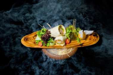 Sıvı azot ile yemekleri sunan. Pide tavuk rulo. Sebze ve salata yaprakları. Yemekler için ahşap tahta. Pide tavuk. Taze salata. Bir dilim limon. Bir cam şişe zeytinyağı.