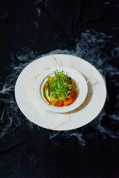 Serving dishes with liquid nitrogen. Salad of vegetables and arugula. Vegetarian dish. Tomatoes and cucumbers. Fresh salad in a white ceramic plate. Dish on a black background.