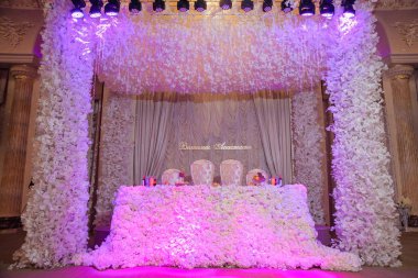 Sofra düğün. Tablo yeni evliler beyaz çiçeklerle süslenmiş. Çiçekler'Arch. Düğün. Mor arka ışık. Düğün süslemeleri.