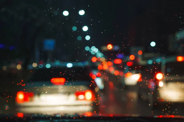 The city lights at night. Rainy weather. Drops on the windshield of the car. The headlights on cars. Night city. Precipitation in the form of rain. Flank.