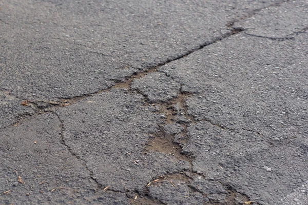 Asphalt road. Cracks and holes in the road. Asphalt. Texture of asphalt coating. Damaged surface. A rift in the road.