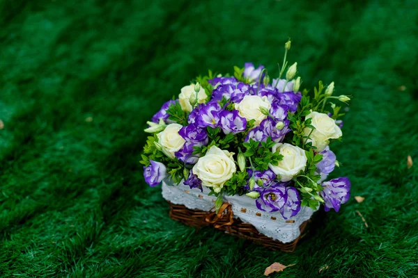Basket with fresh flowers. The flowers are purple and white. Floristic. Green lawn. Wicker basket.