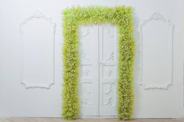 Bahar dekoru. Beyaz duvarlar. Duvarların üzerinde güzel bir alçı var. Yeşil ve beyaz çiçekler kemeri. Fotoğraf bölgesi. Çiçek ile kapı dekor. Beyaz bebeğin nefesi.