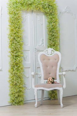 Bahar dekoru. Beyaz duvarlar. Duvarların üzerinde güzel bir alçı var. Yeşil ve beyaz çiçekler kemeri. Çiçek ile kapı dekor. Beyaz bebeğin nefesi. Sandalyenin soluk pembe bir rengi vardır. Düğün buketi.