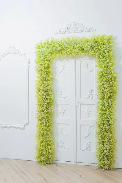 Spring decor. White walls. Beautiful stucco on the walls. Arch of green and white flowers. Photo zone. The decor of the doorway with flowers. White baby\'s breath.