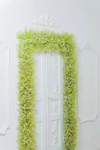 Spring decor. White walls. Beautiful stucco on the walls. Arch of green and white flowers. Photo zone. The decor of the doorway with flowers. White baby\'s breath.