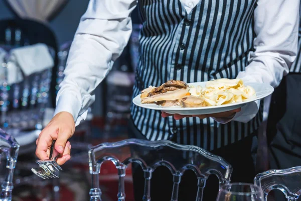 The waiter lays out a dish from a plate. Service personnel. The event at the restaurant. Festive table setting.