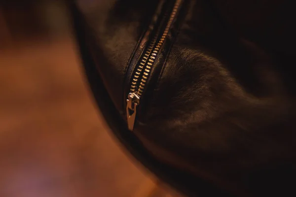Lock on black leather bag. A black bag lies on the wooden floor. Texture of metal zipper on the bag.