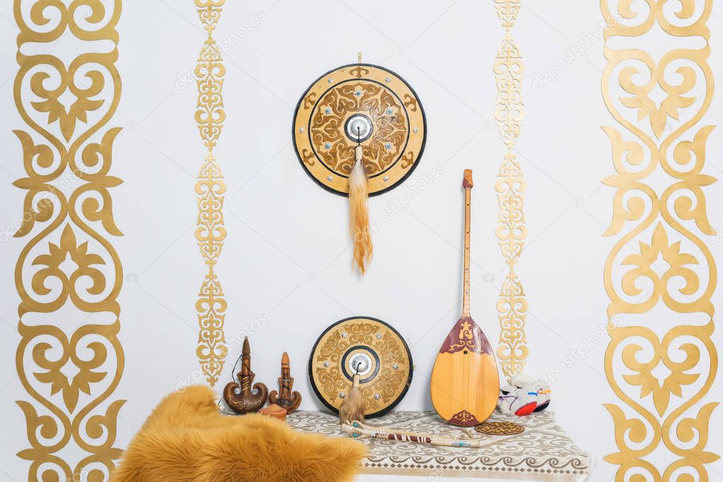 Gold ornaments on the white walls. Sheep skin decorative. A two-stringed Kazakh national musical instrument dombra. Leather container for storing drinks. Kazakh medieval shield.