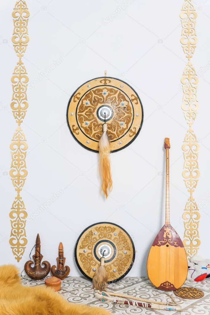 Gold ornaments on the white walls. Sheep skin decorative. A two-stringed Kazakh national musical instrument dombra. Leather container for storing drinks. Kazakh medieval shield.