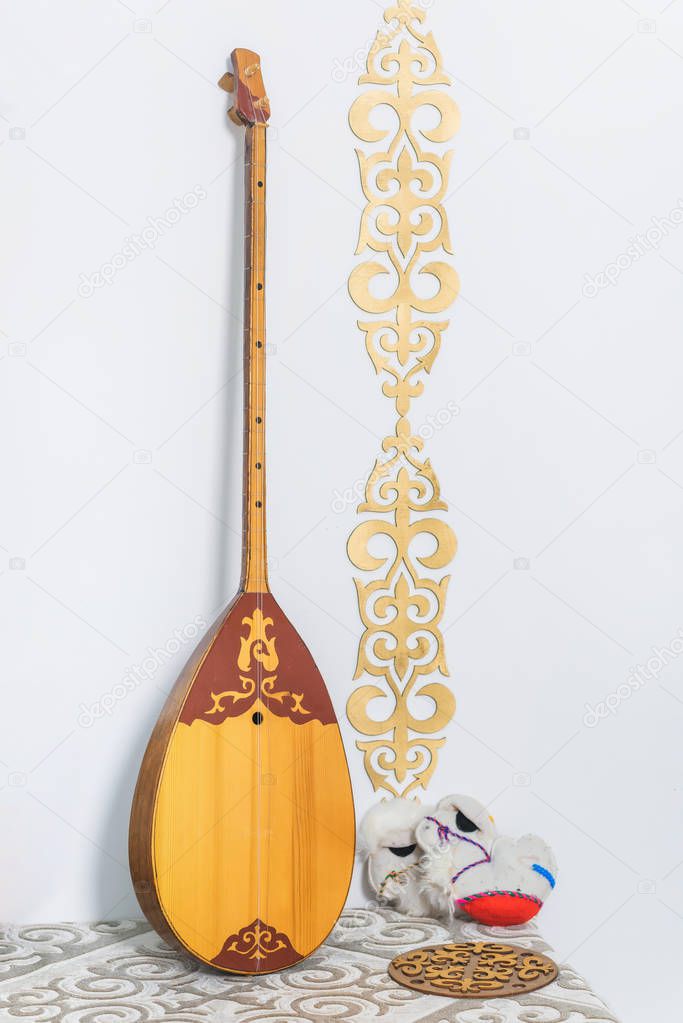 Gold ornaments on the white walls. Wooden chest. Kazakh national souvenir in the form of a camel. Felt toy. Souvenir camel made of wool. A two-stringed Kazakh national musical instrument dombra.