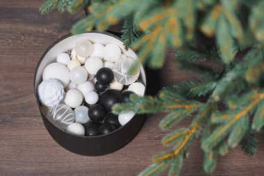 Noel ağacı. Laminat şeklinde linolyum. Noel süslemeleri ile siyah yuvarlak kutu. Yuvarlak oyuncaklar siyah beyaz. İğne yapraklı bitkilerin dekoru.