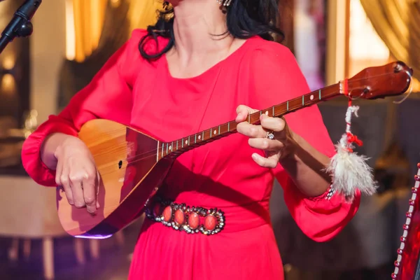 Kırmızı elbiseli bir kadın kazak Ulusal müzik aleti çalıyor. Yaylı enstrüman dombra.