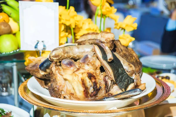 Traditional Kazakh dish of lamb. Roast lamb. Meat dish. Festive table setting. Fruits. Table decor with fresh flowers. Guests at the table. Plates. Tableware.