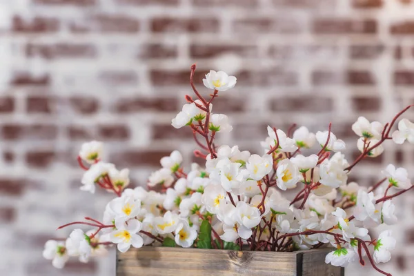 White flowers in a wooden box. Table covered with white tablecloth. Brick wall texture. The interior of the room. Lights on the wire hanging on the wall. Decorative brick wall.