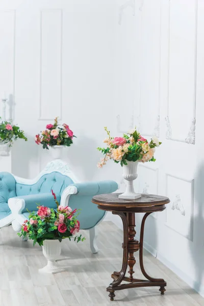 Bouquet of roses. Flowers in white vase. Room decor plants. Stucco work on the white walls. Spring photo zone. Wooden vintage table. Blue couch. White vases on columns.