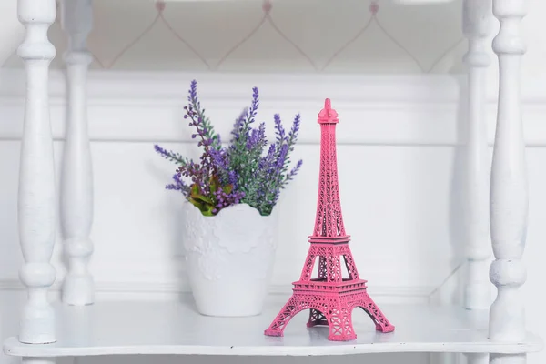 Vintage wooden bookcase in the background of bright walls. White pots of lavender. Room decor flowers. Pink figure of the Eiffel tower.